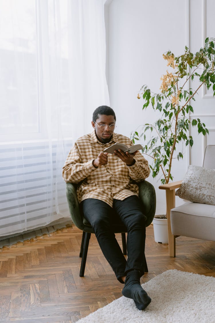 A Man Sitting On A Chair While Reading A Book