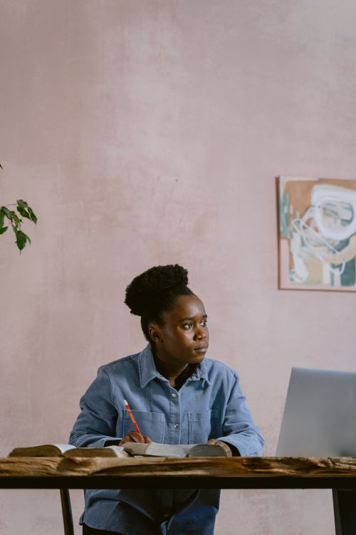 Free An adult working intently at a desk in a home setting, surrounded by books and art. Stock Photo