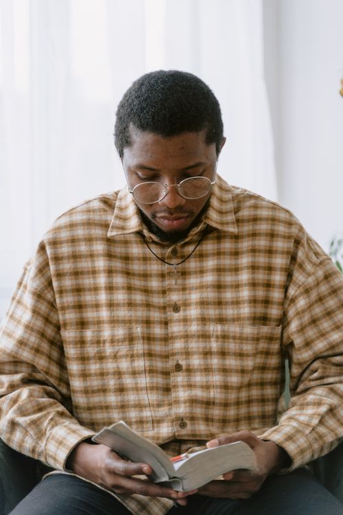Free African American man in plaid shirt reading a book indoors, wearing eyeglasses. Stock Photo