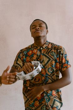 African American man wearing floral shirt enjoying music with a tambourine indoors.