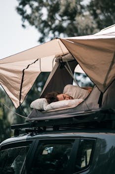 A person peacefully sleeps in a rooftop tent on an SUV, enjoying nature outdoors.