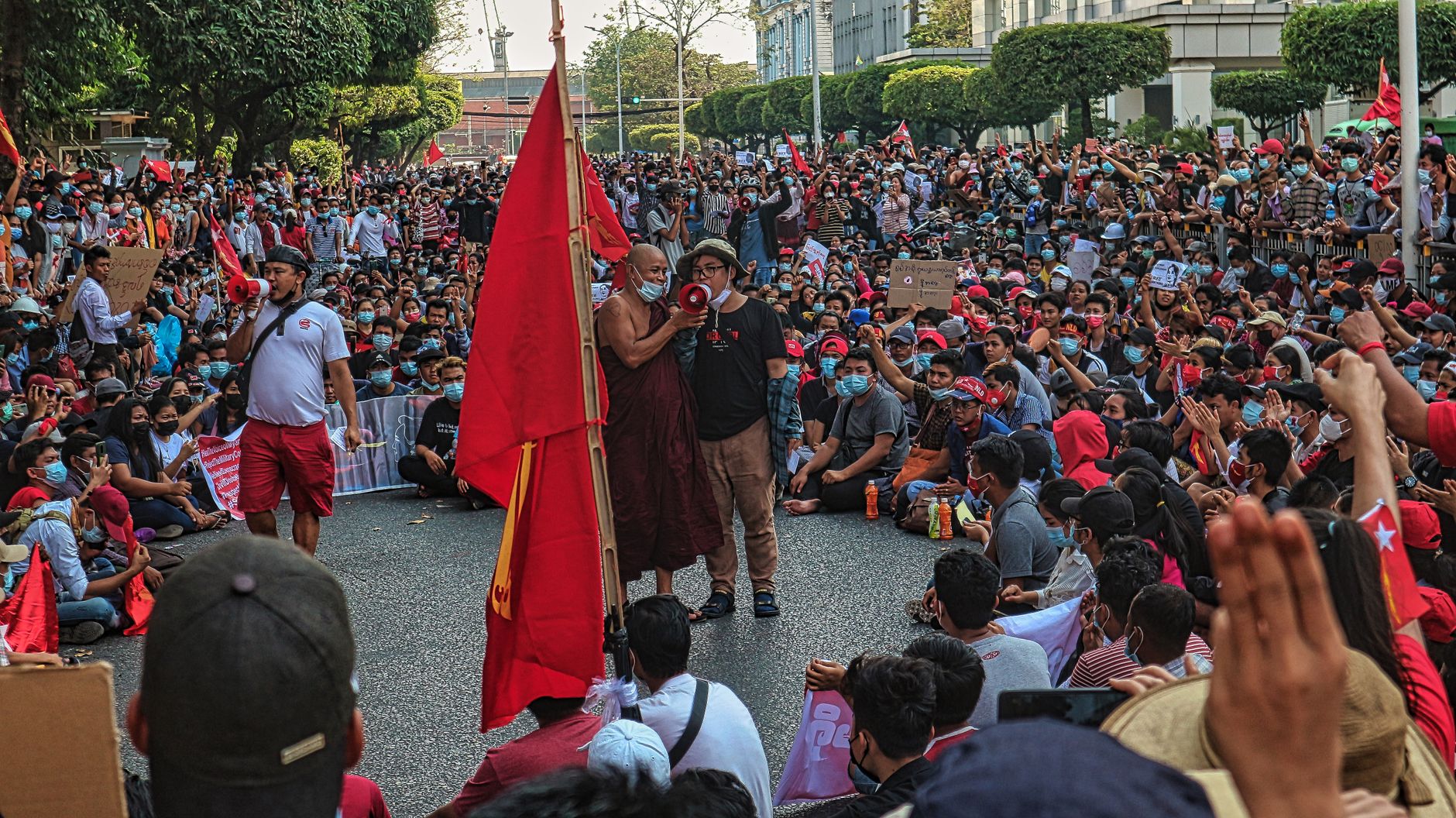 A large crowd gathers in Yangon, Myanmar for a peaceful protest with vibrant red flags.