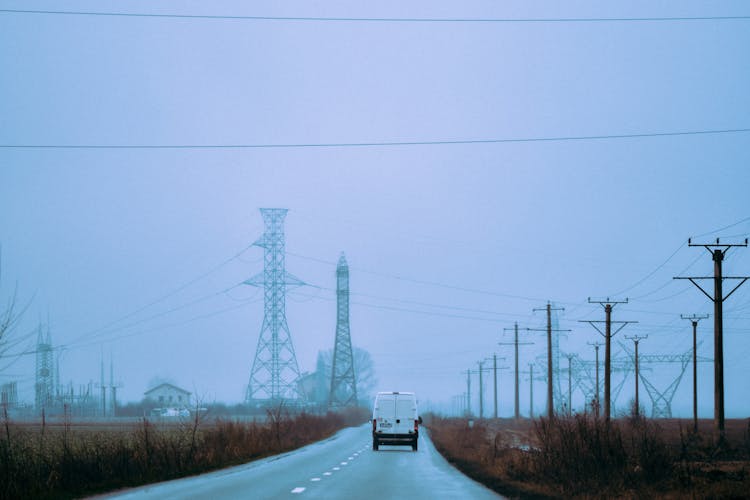 Minivan Driving On Road Between Electric Towers In Autumn