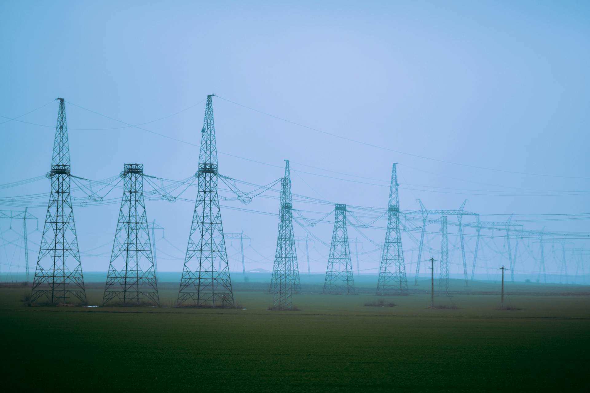 A row of transmission towers stretches across a foggy rural field, exemplifying industrial energy distribution.