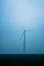 Row of air generators with vanes on terrain under blue sky in fog in evening