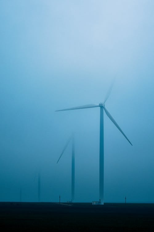 Free Row of air turbines producing electric energy on land under foggy sky in twilight Stock Photo