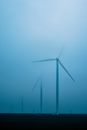 Row of air turbines producing electric energy on land under foggy sky in twilight