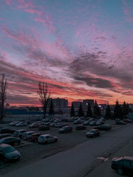 Narrow road and parked automobiles on pavement under colorful sky with fluffy clouds in evening town