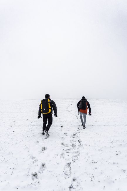 Two hikers trek through a serene snow-covered landscape on a winter day.