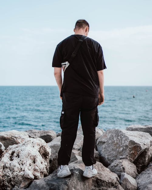 Man in Black T-shirt and Black Pants Standing on Rocky Coast