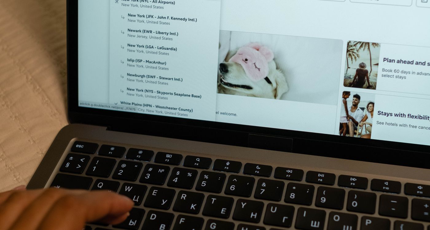 Person booking travel on a laptop and phone, searching flights and hotels