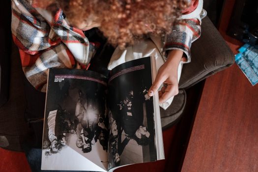 A person in a plaid shirt reads a magazine in a comfortable indoor chair. - Fotografer Sidoarjo