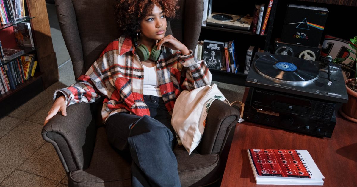 A person sitting by a window with headphones on, eyes closed, holding a vinyl record sleeve