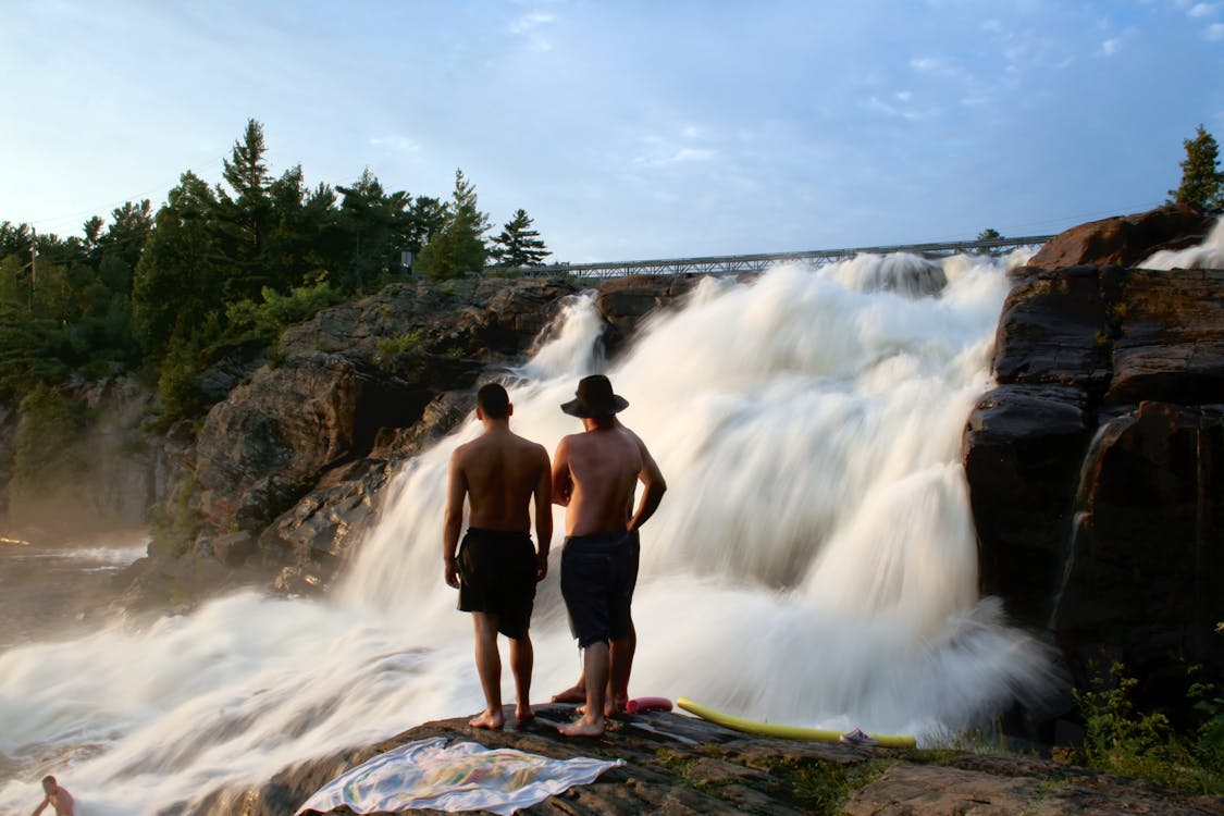 免費 三人站在看岩石的瀑布 圖庫相片