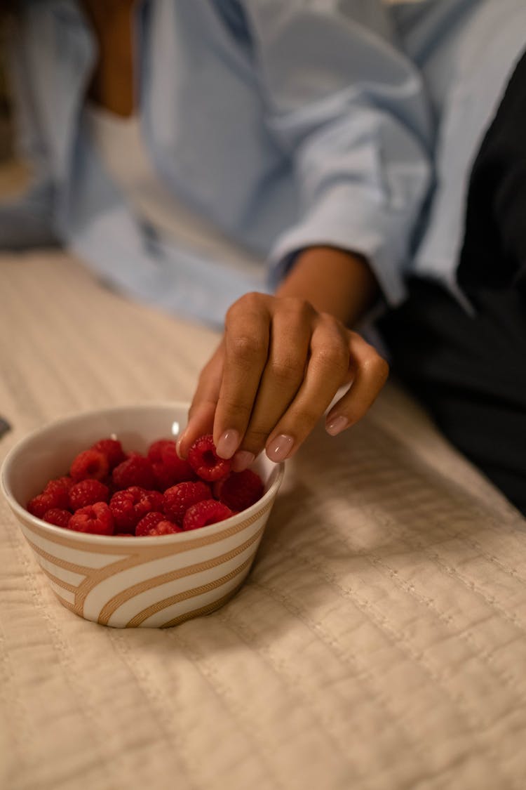 A Person Getting Red Raspberries From A Bowl