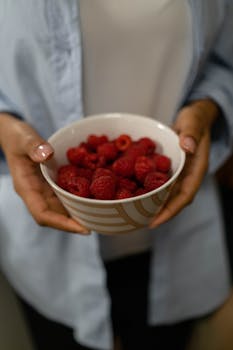 Close-up image of a person holding a bowl filled with fresh, organic raspberries.