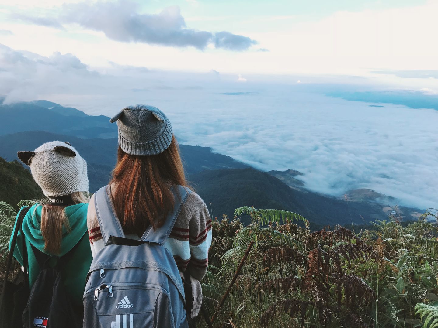 Due donne con lo zaino ammirano un panorama montano avvolto dalle nuvole, ideale per chi ama viaggiare