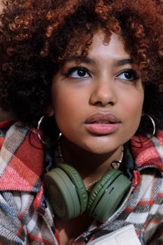 African-American woman with curly hair wearing headphones, looking thoughtful indoors.