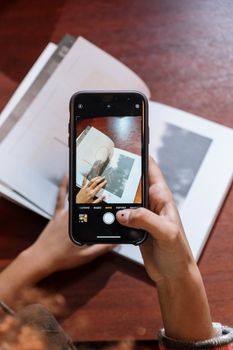 Person photographing a book with a smartphone indoors on a wooden table.