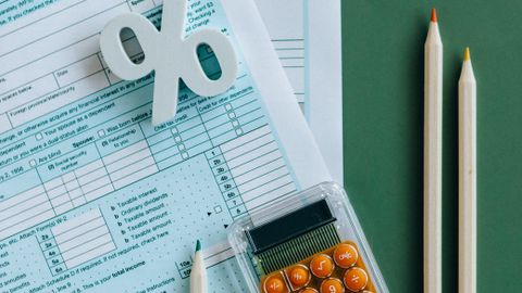 Flat lay of tax documents, calculator, and pencils on green surface.