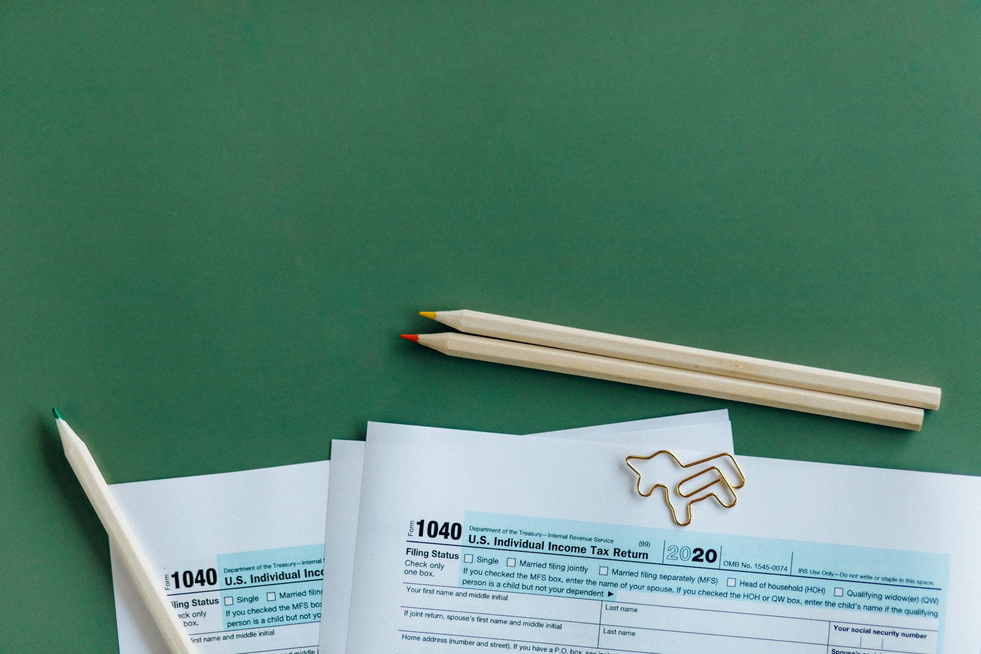 1040 tax form with colored pencils and paperclip on green background.