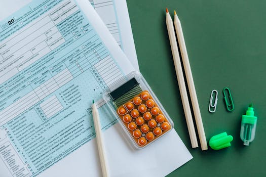 Flat lay of tax forms, calculator, pencils, and clips on green surface, ideal for finance or accounting themes.