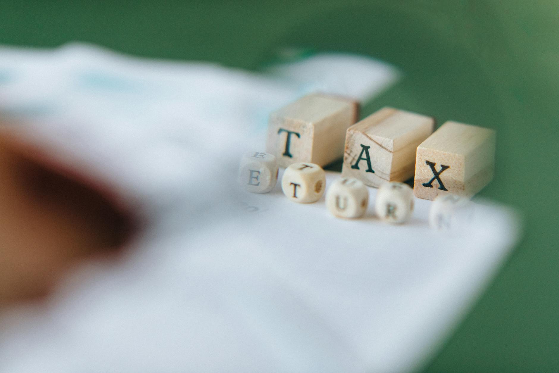 Wooden blocks and dice spelling 'Tax Return' on a blurred green background.