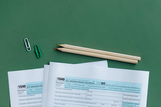 U.S. tax forms with pencils and paperclips on green surface in a flat lay setup.