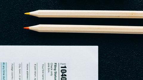 Wooden pencils and 1040 tax form on black background with tiles spelling 'TAXES'.