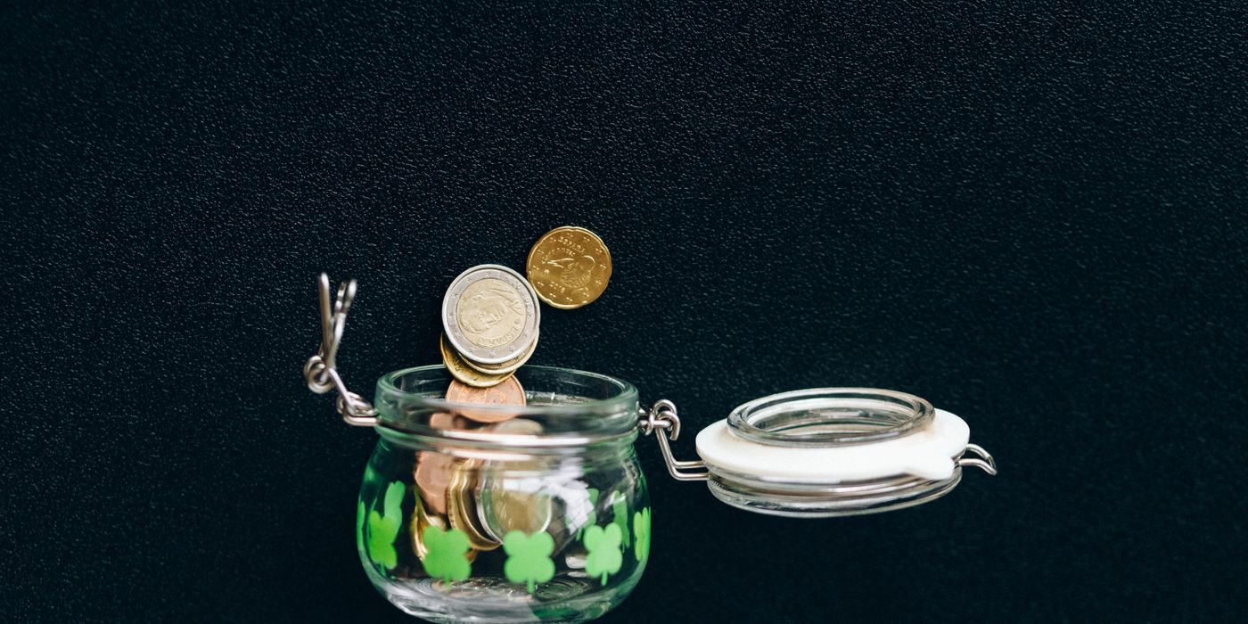 Glass jar with coins falling into it on a black background, symbolizing savings.