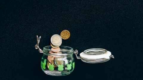 Glass jar with coins falling into it on a black background, symbolizing savings.