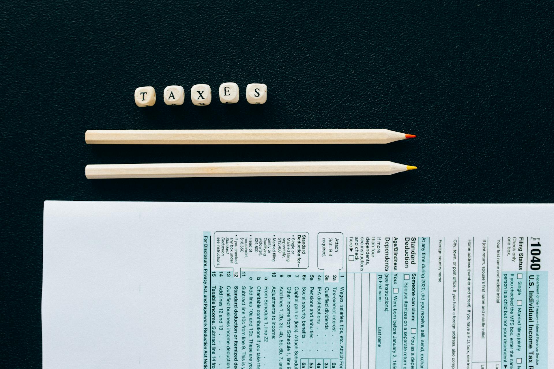 Flat lay of 1040 tax form with pencils and 'TAXES' blocks on black background.