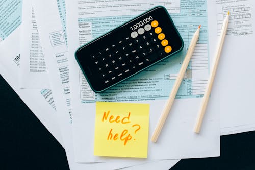 Free Top view of financial papers with a calculator, pencils, and a note saying 'Need help?' indicating tax or accounting assistance. Stock Photo