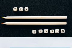 Creative composition featuring 1040 tax form, pencils, and letters spelling 'Tax Season' on black background.