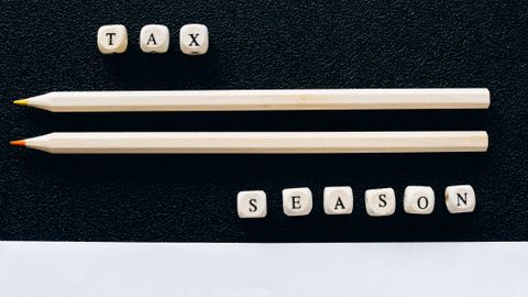 Creative composition featuring 1040 tax form, pencils, and letters spelling 'Tax Season' on black background.
