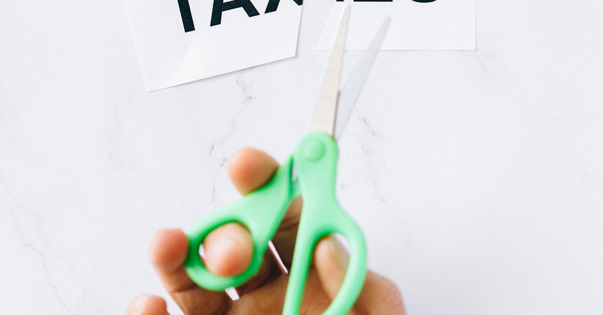 Photo by Nataliya Vaitkevich Top-down view of a hand holding scissors cutting the word 'taxes' on a marble surface.