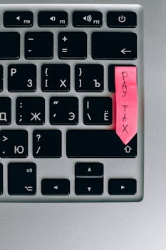 Tax payment reminder on pink sticky note placed on a laptop keyboard.