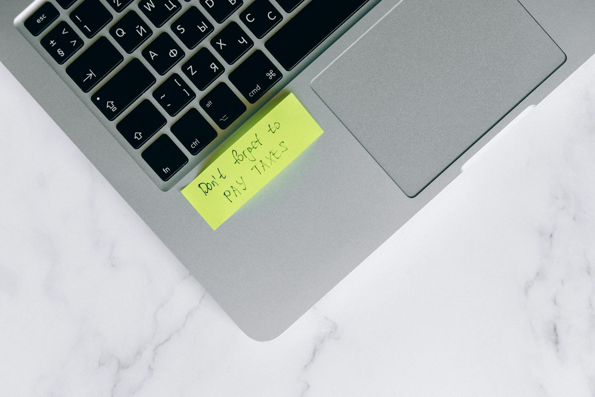 Close-up of a sticky note on a laptop reminding to pay taxes, emphasizing tax season.