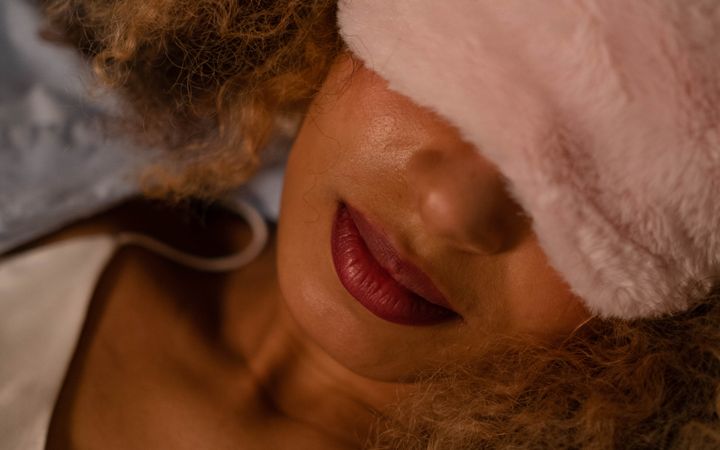 A serene portrait of an adult woman wearing a pink sleep mask, lying down and relaxing indoors.