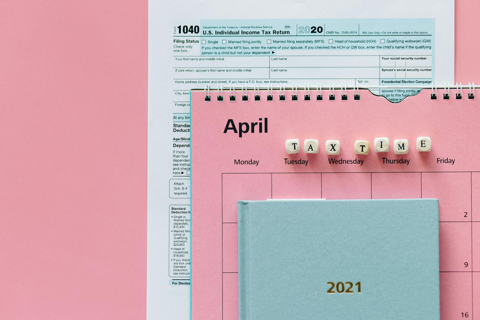 Flat lay image of tax forms, calendar, and 'tax time' reminder on a pink background.
