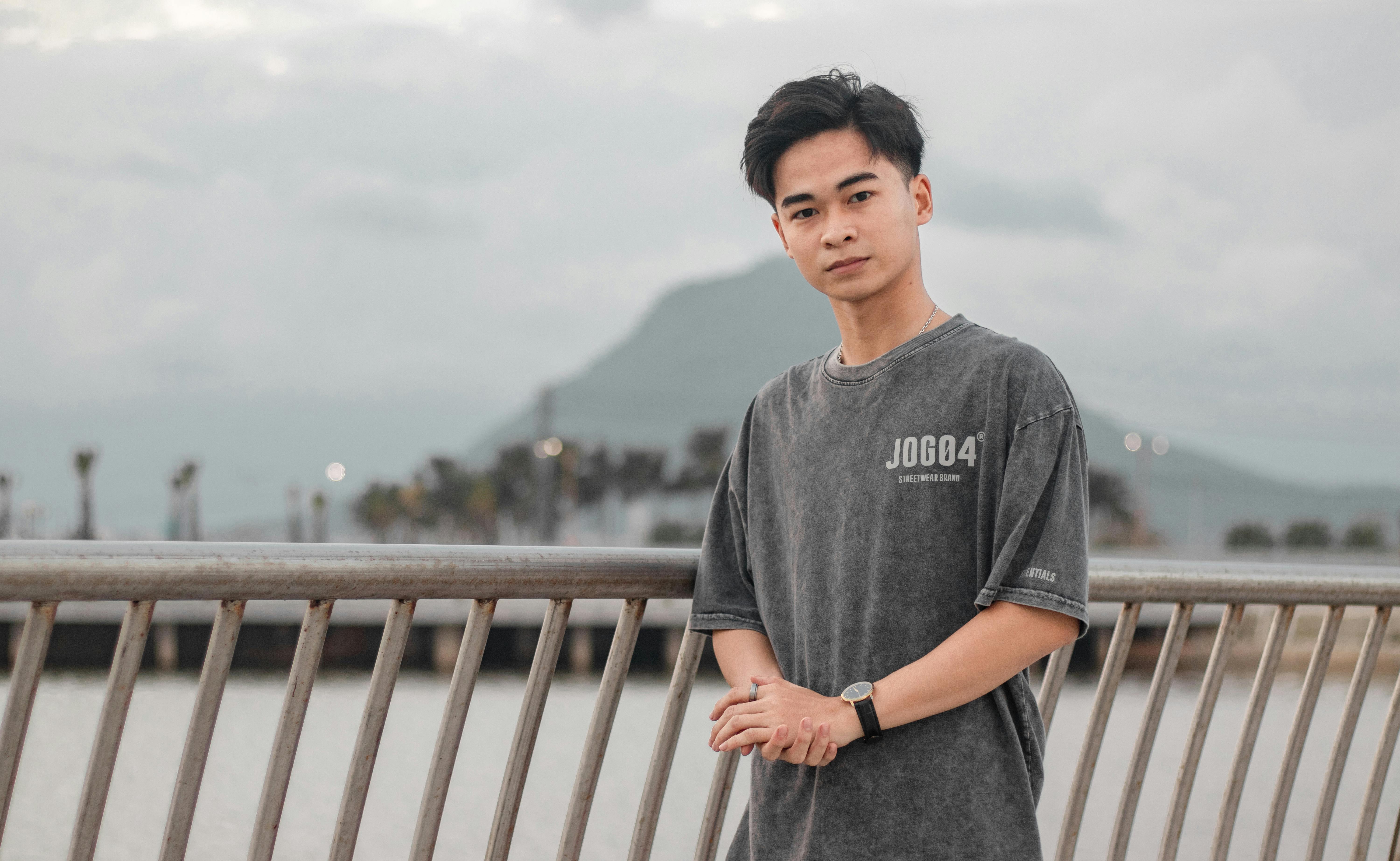 Portrait of a young man with hands together posing outdoors by a lake with railings in a serene setting.