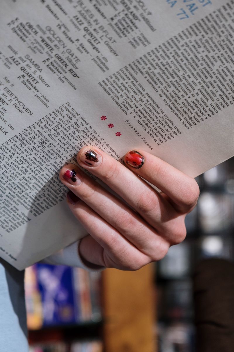 Mano sosteniendo una página impresa con manicura de tonos tinta y rojo difuminado