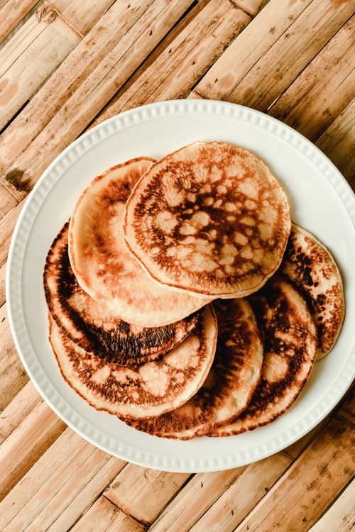 Free A stack of golden pancakes served on a white plate with a rustic wooden backdrop. Stock Photo
