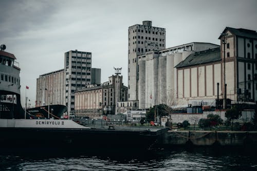 Modern big cruise ship moored on rippling water in harbor in city with residential buildings on street against overcast sky