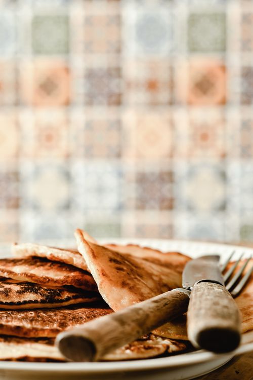 Free A stack of golden pancakes with wooden handle cutlery on a plate, set against a colorful tiled background. Stock Photo