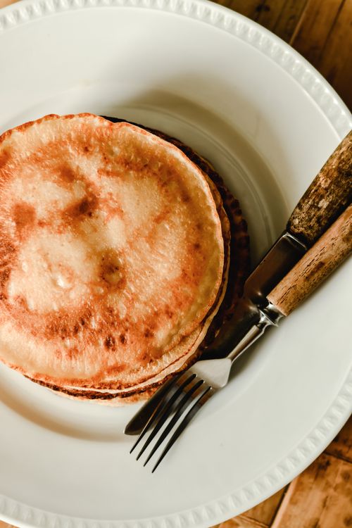 Free Delicious stack of pancakes served on a ceramic plate with wooden utensils, perfect for a cozy breakfast. Stock Photo