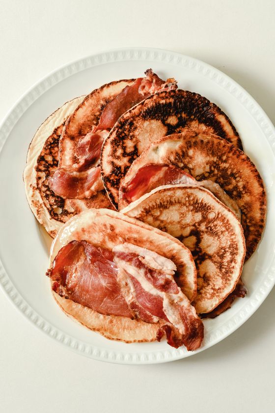 Overlapping golden buttermilk pancakes layered with crispy streaky bacon on a white plate