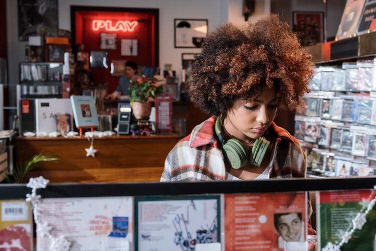 Young Curly Woman With Headphones Choosing A CD In A Music Store