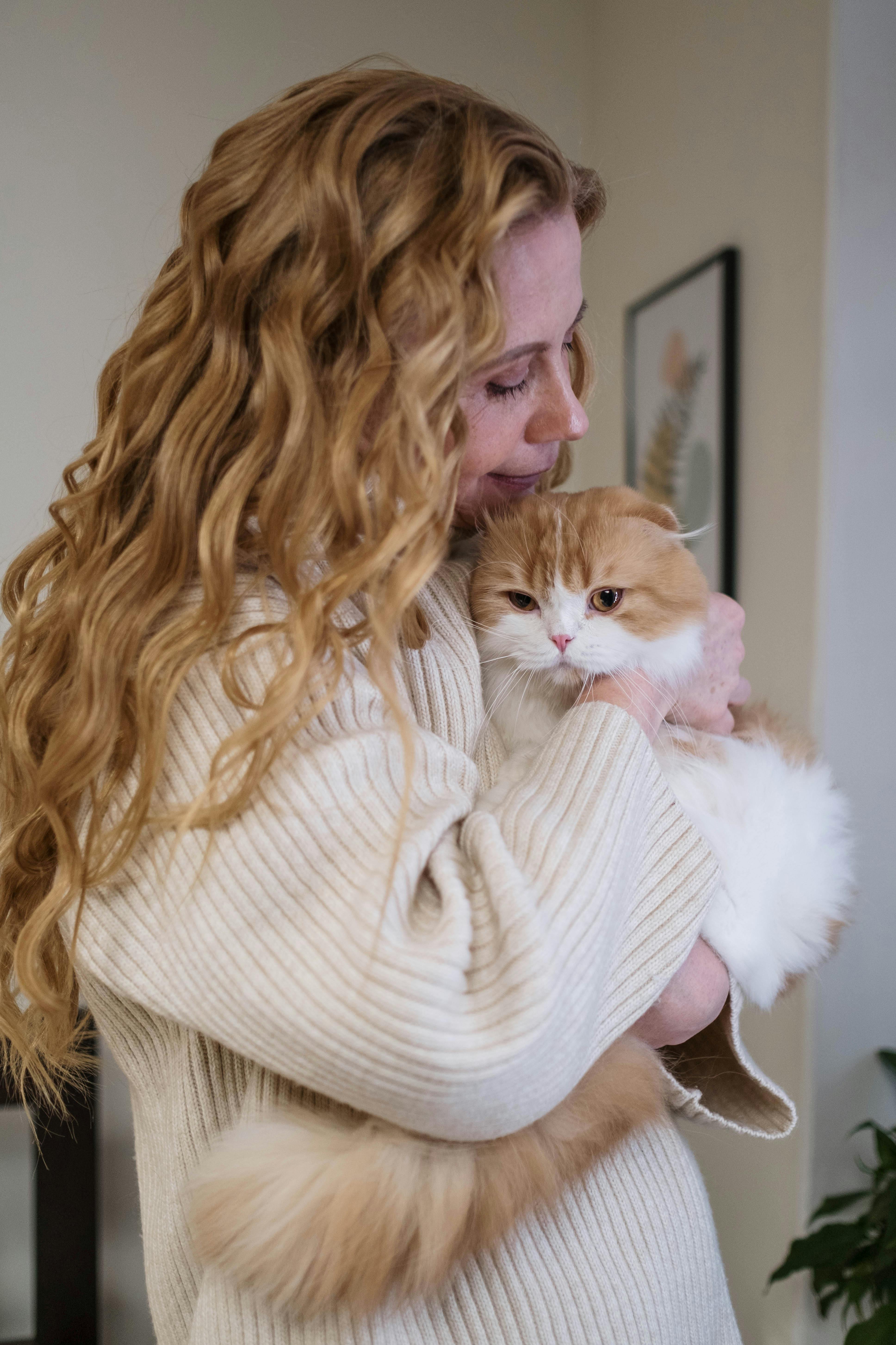 woman in white knit sweater holding white and orange cat