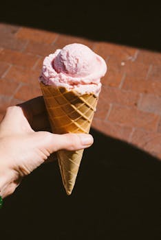Close-up of a hand holding a strawberry ice cream cone outdoors on a sunny day.